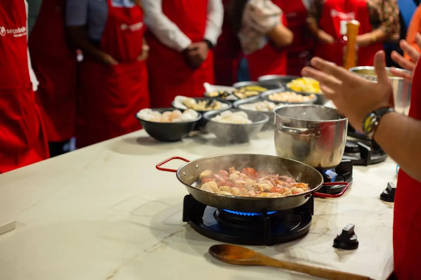 Group in aprons around a cooktop during a cooking class