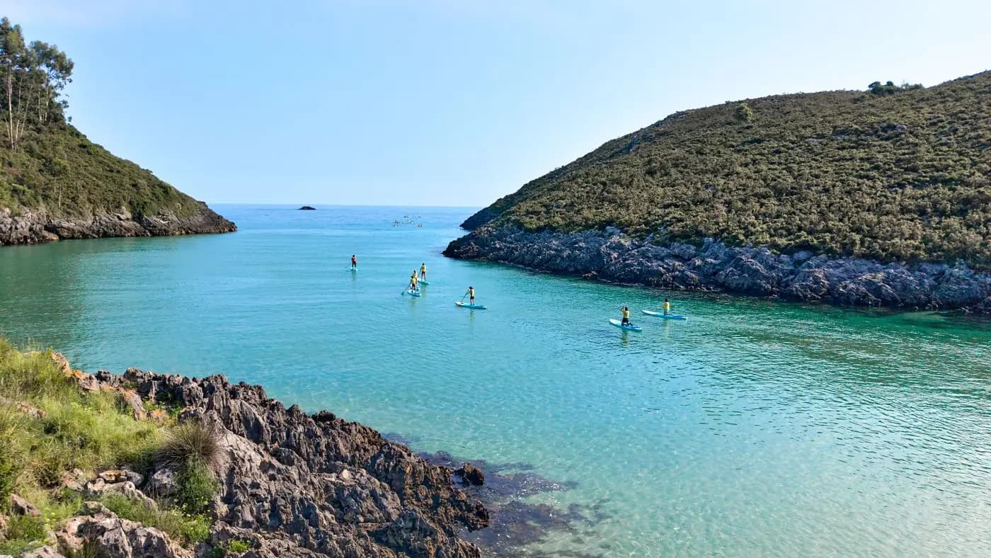 Group paddleboarding in a calm turquoise bay between hills