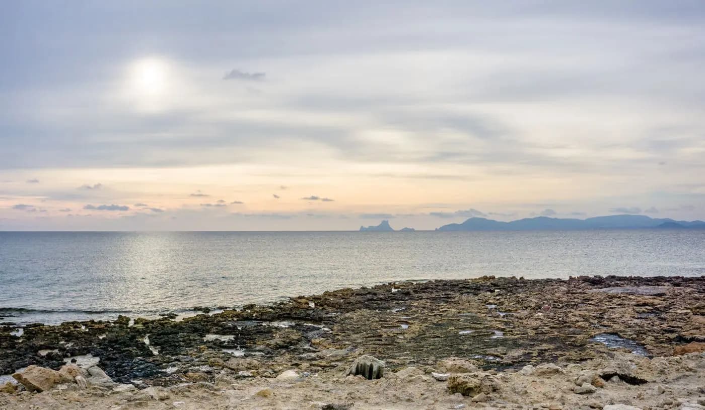 Rocky coast at sunset with Es Vedrà islet on the horizon