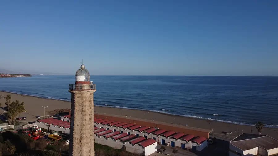 White lighthouse and beach in Estepona, red-roofed cabins