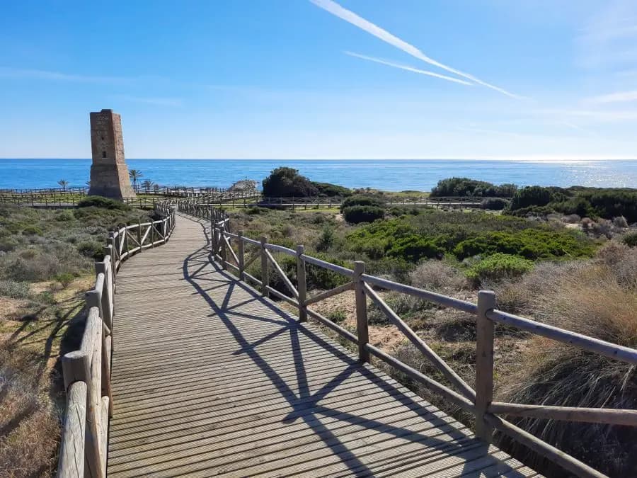 Sunlit boardwalk leading to a historic tower on the Marbella coast