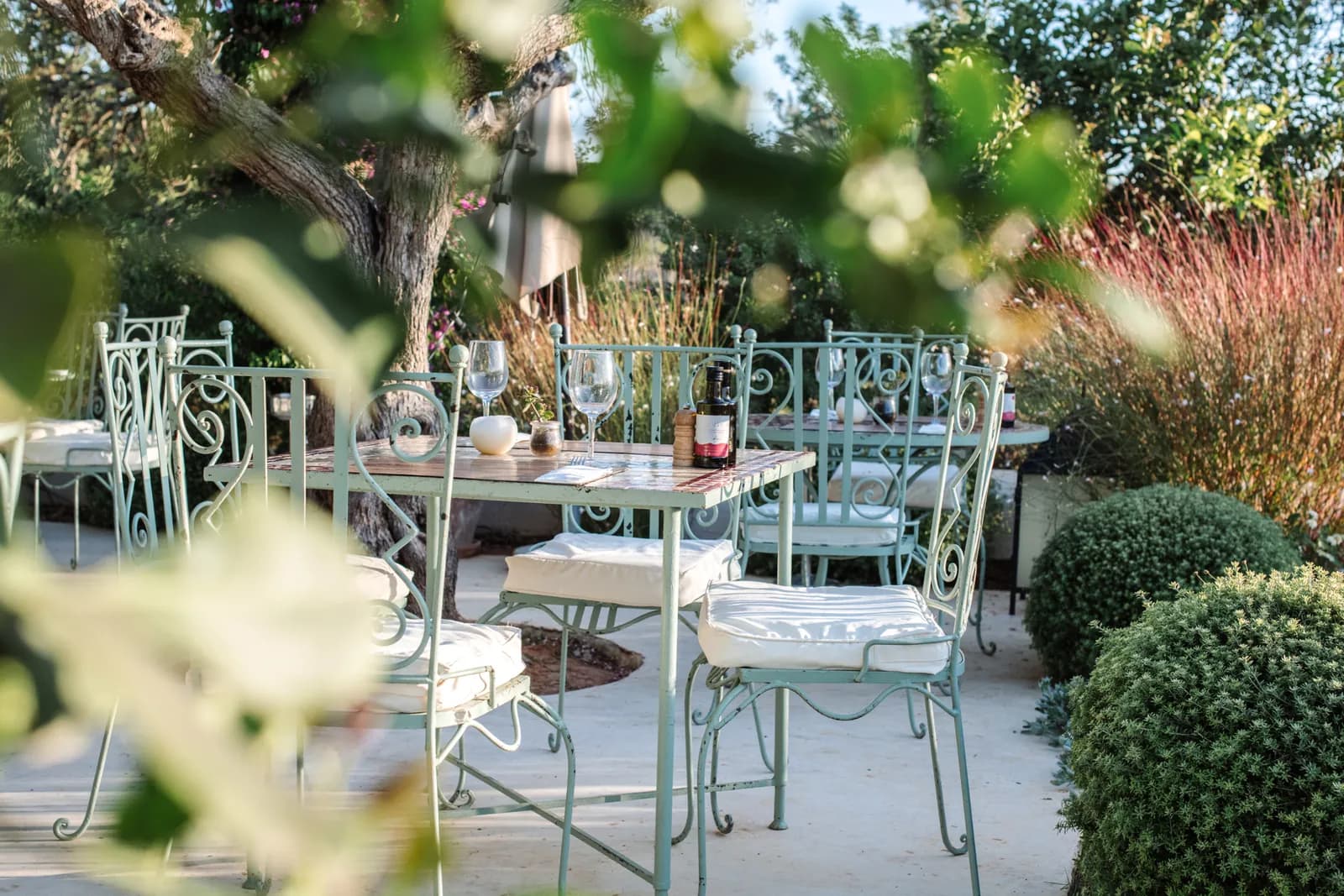 Terrace tables under trees and wrought-iron chairs at Aubergine by Atzaró in Ibiza