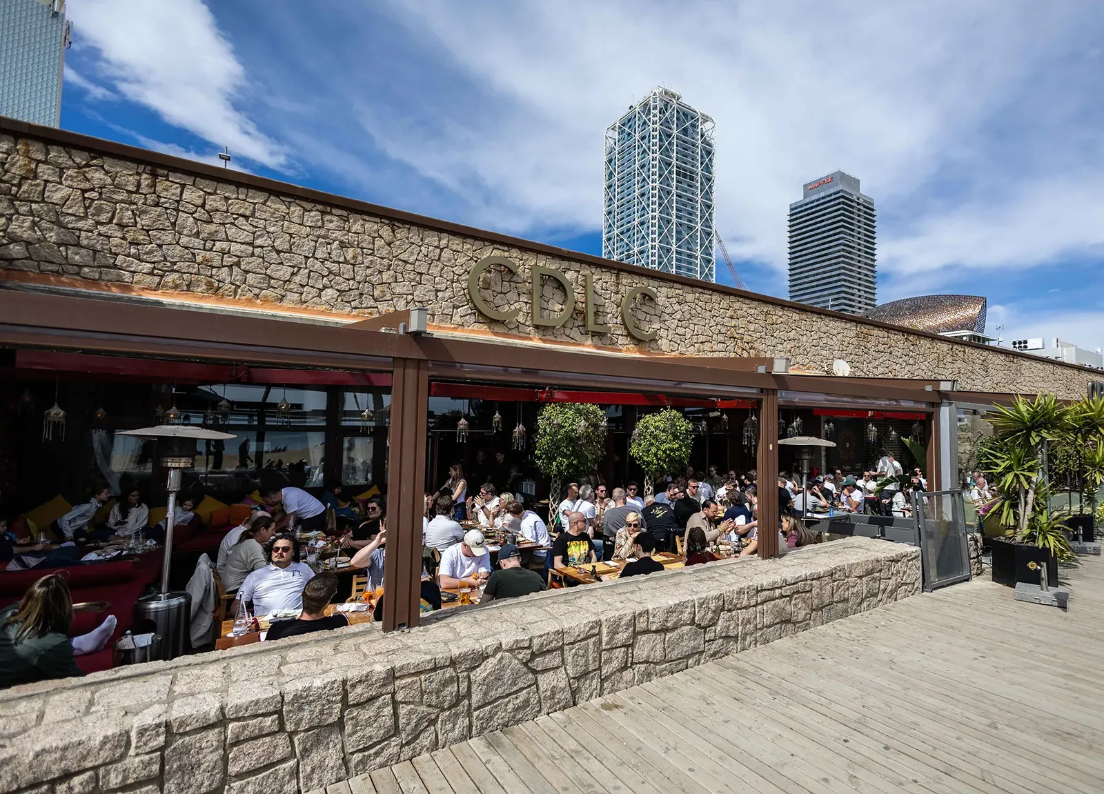 Carpe Diem Lounge Club terrace with guests at tables and Barceloneta towers in the background