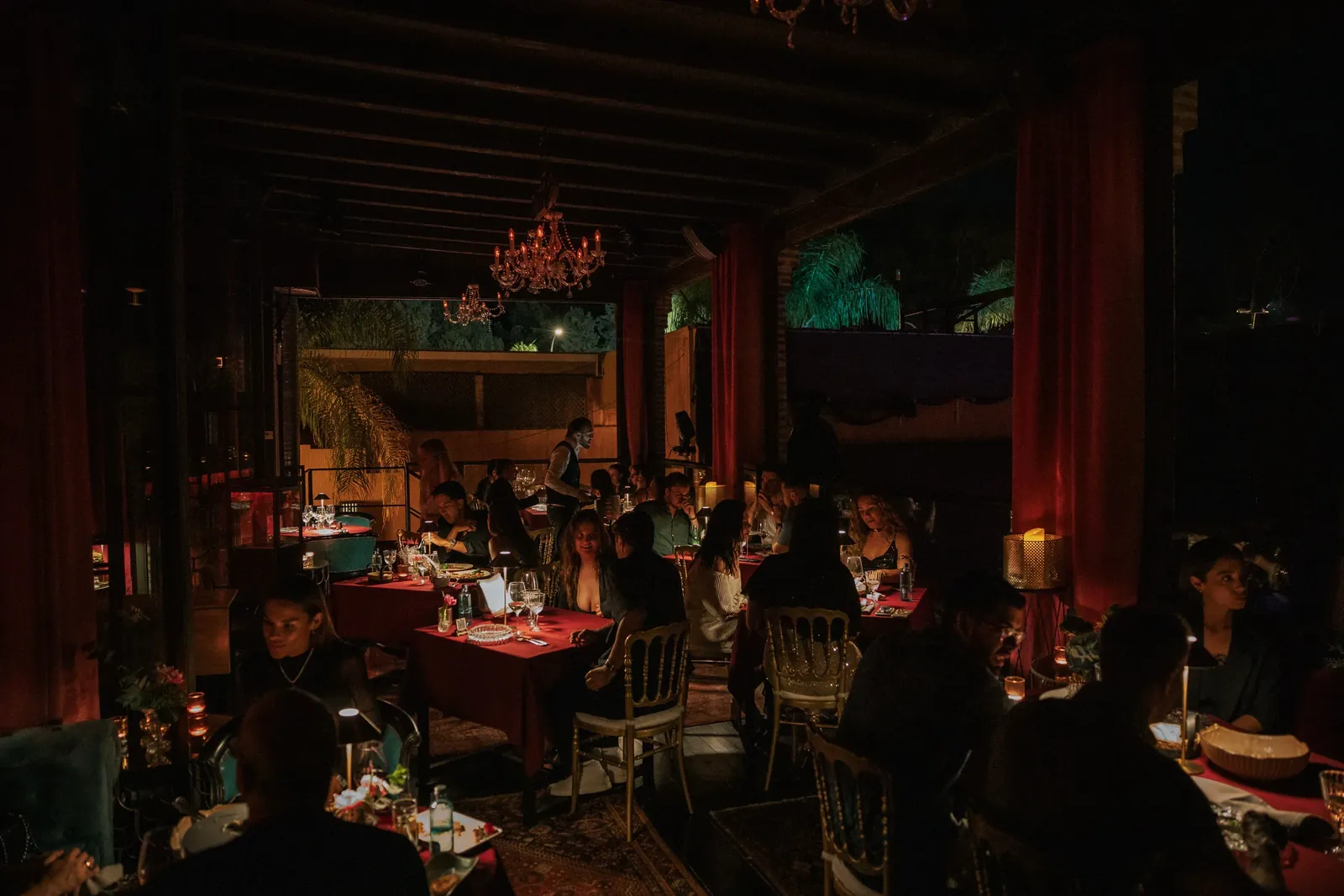 Dimly lit dining room at LØV Marbella with red curtains and laid tables