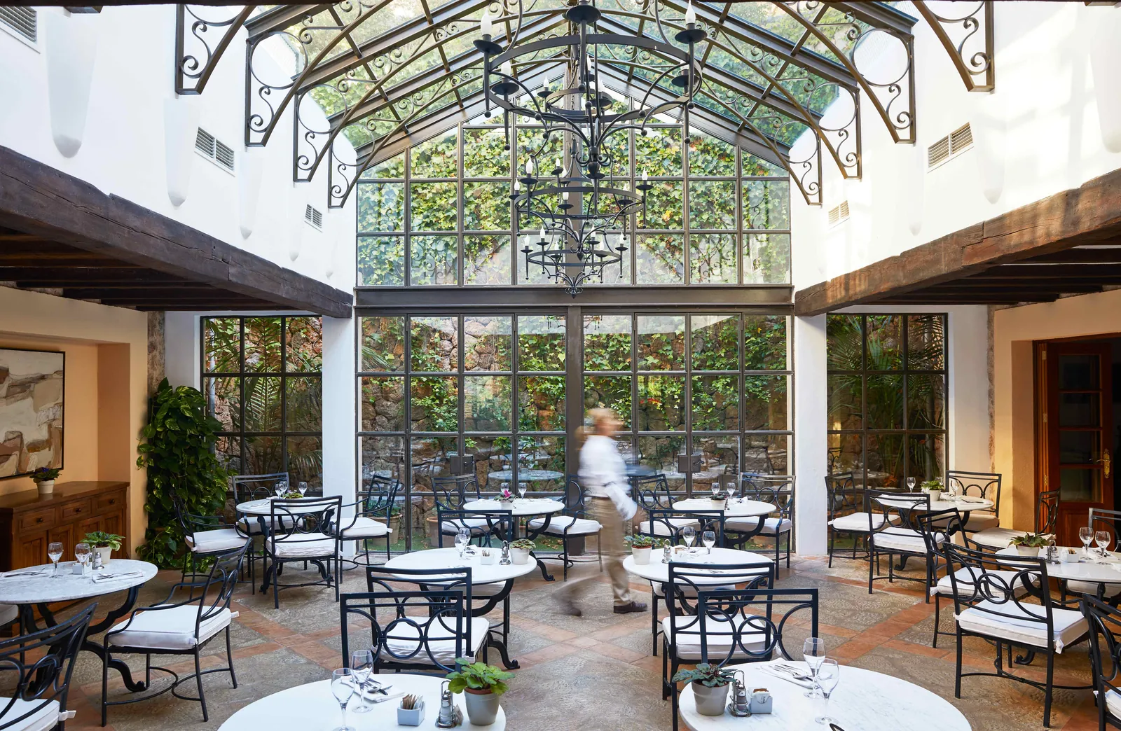 Dining room of La Residencia restaurant with glass roof and round tables in Deià