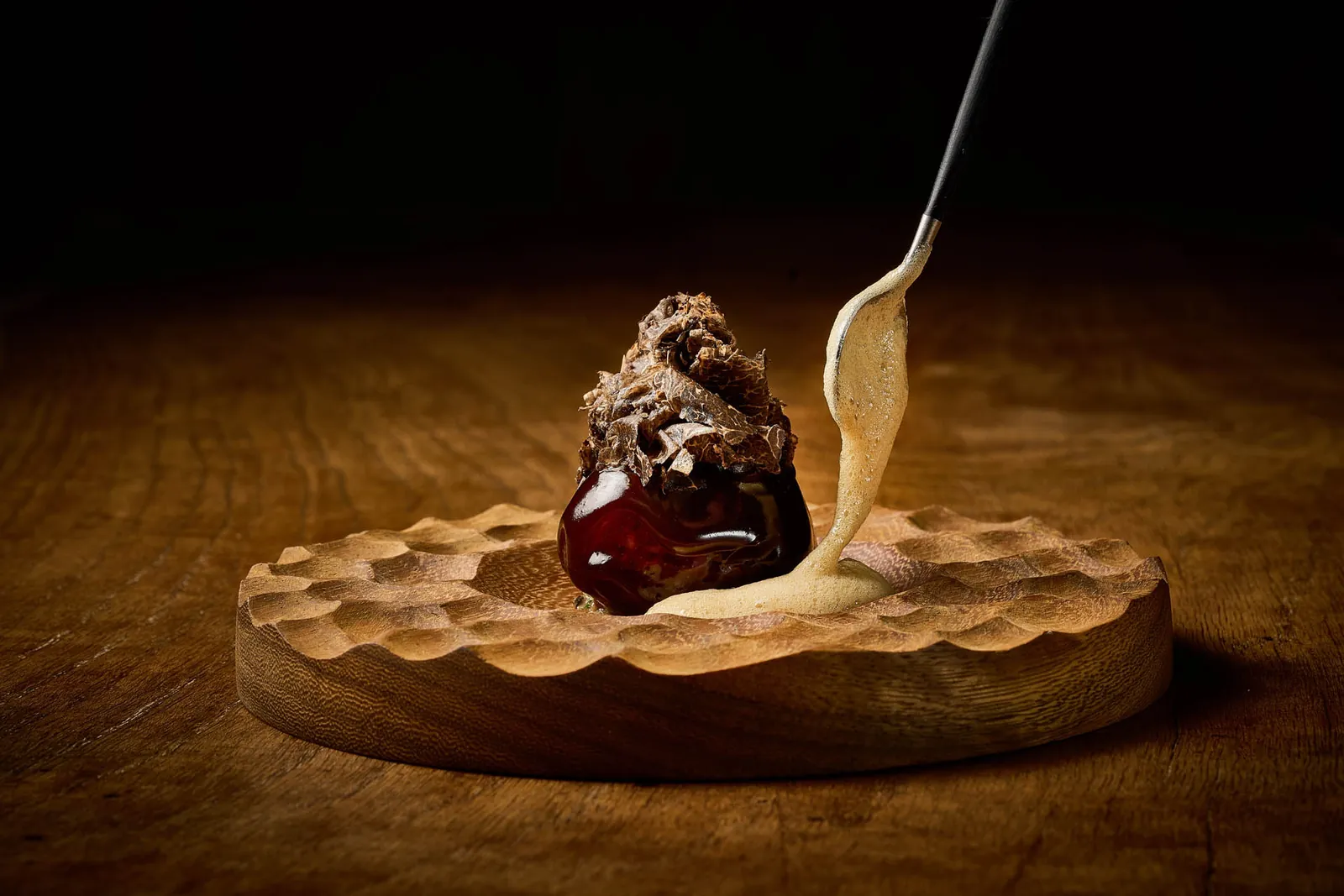 Dark dish served on a wooden board with a spoon at Azurmendi