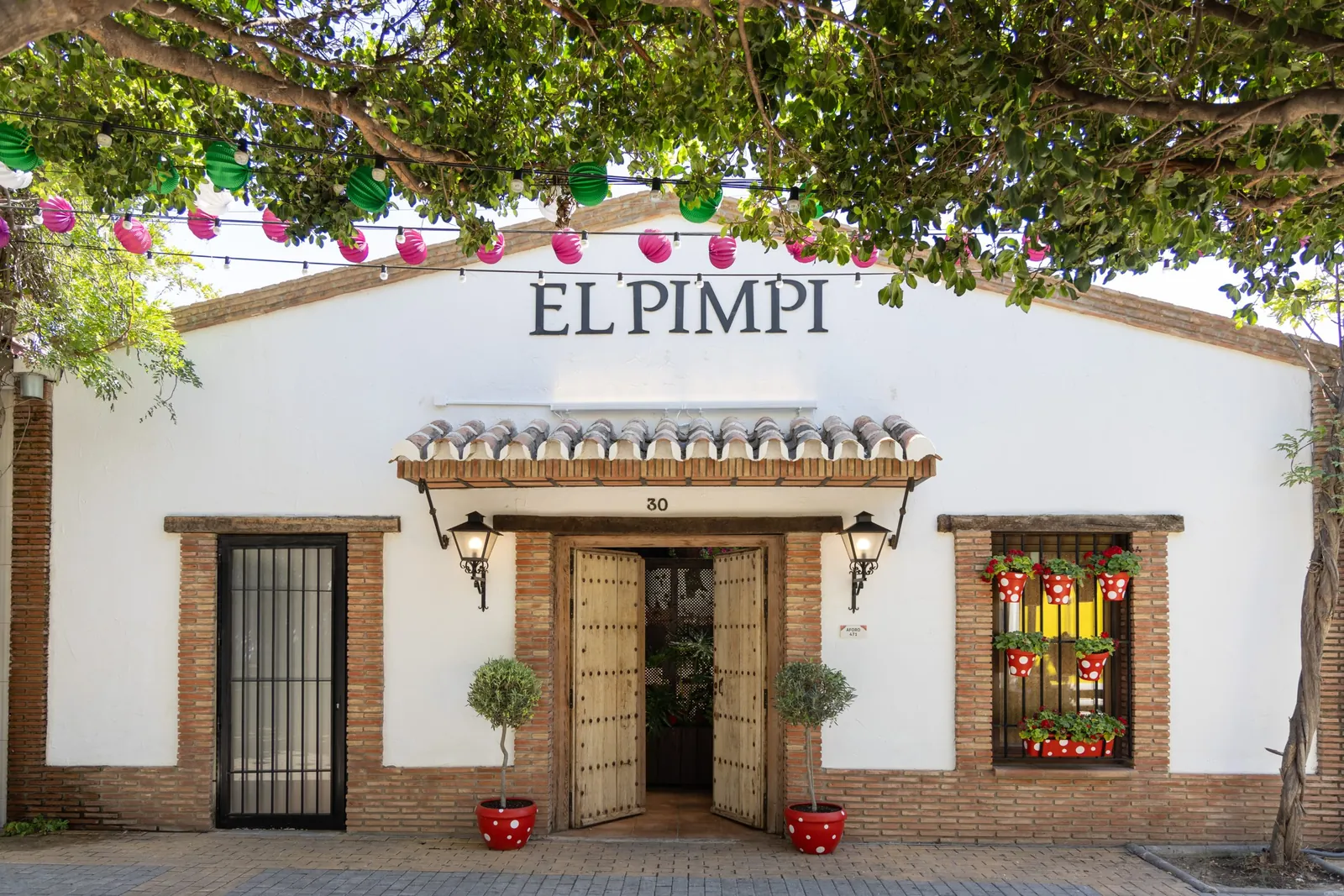 White façade of El Pimpi restaurant in Málaga with sign under trees