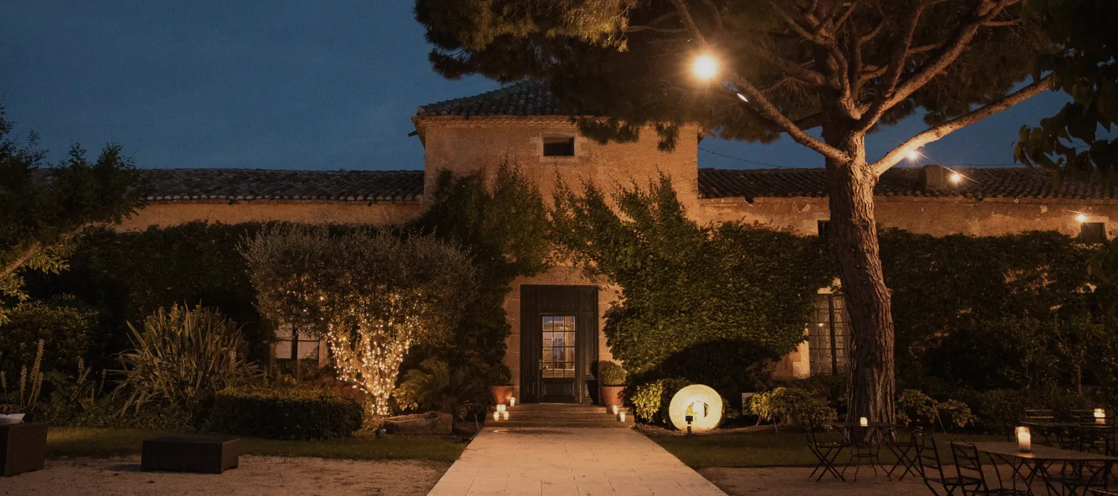Facade of La Torre dels Lleons lit at night, pathway and garden